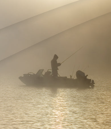 Silhouette of a person fishing from a boat on a calm body of water.